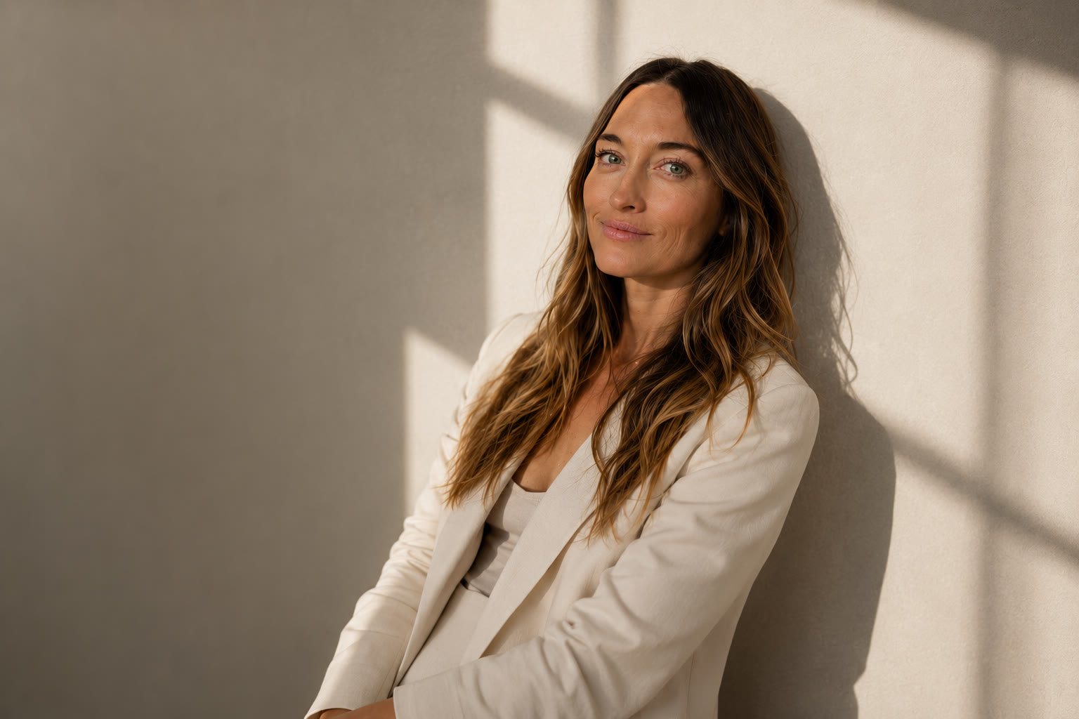 Lauren LoBue in a cream blazer leaning against a sunlit wall